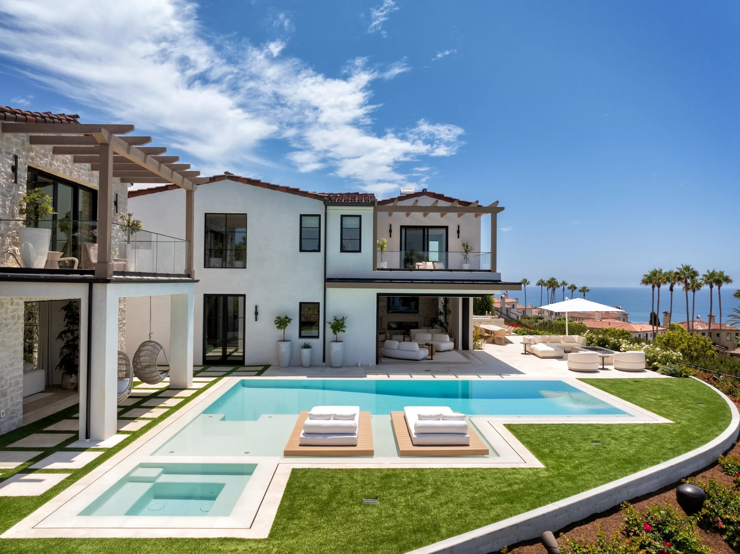 A zero-edge pool and spa surrounded by lawn with an expansive Pacific Ocean view