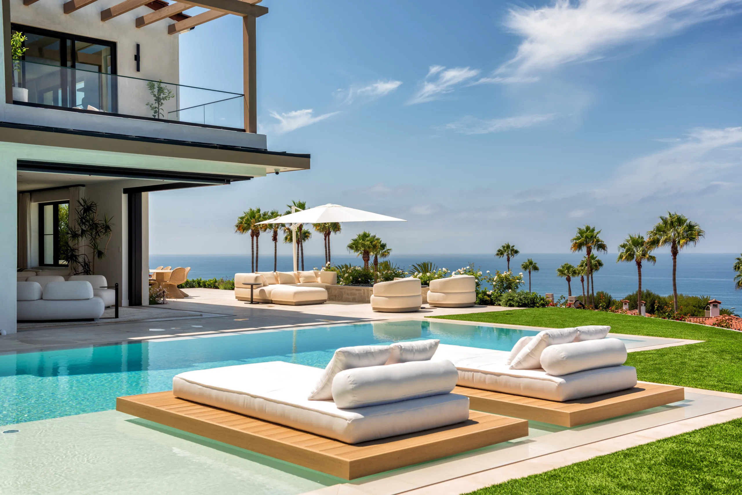 Pool with two floating daybeds, outdoor seating, palm trees, and ocean views