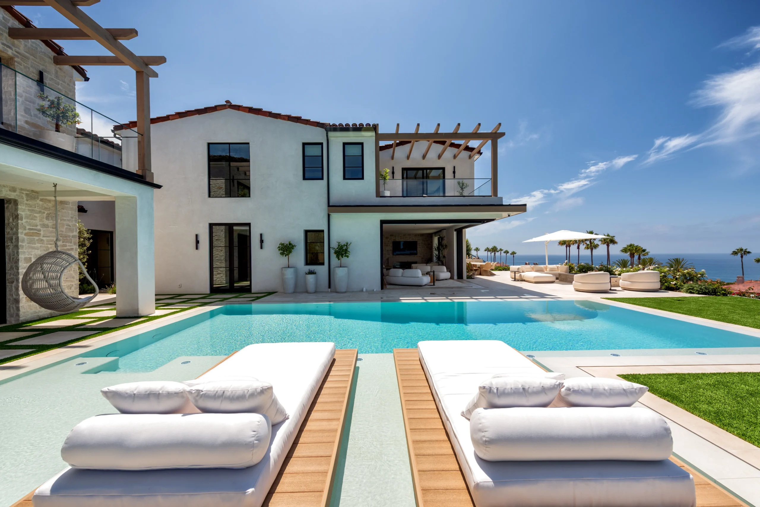 An organic modern pool, daybeds, covered lounge, and ocean view